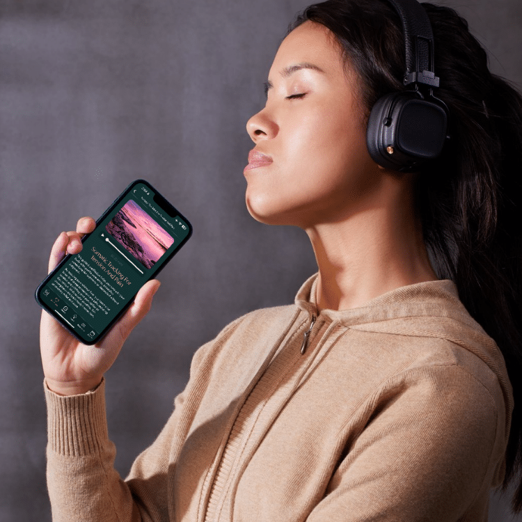 Woman wearing over-ear headphones, eyes closed, enjoying music while holding a smartphone close to her face.