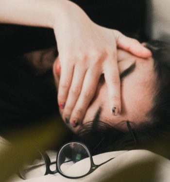 Woman lying on bed covering her head with her hand, stressed out